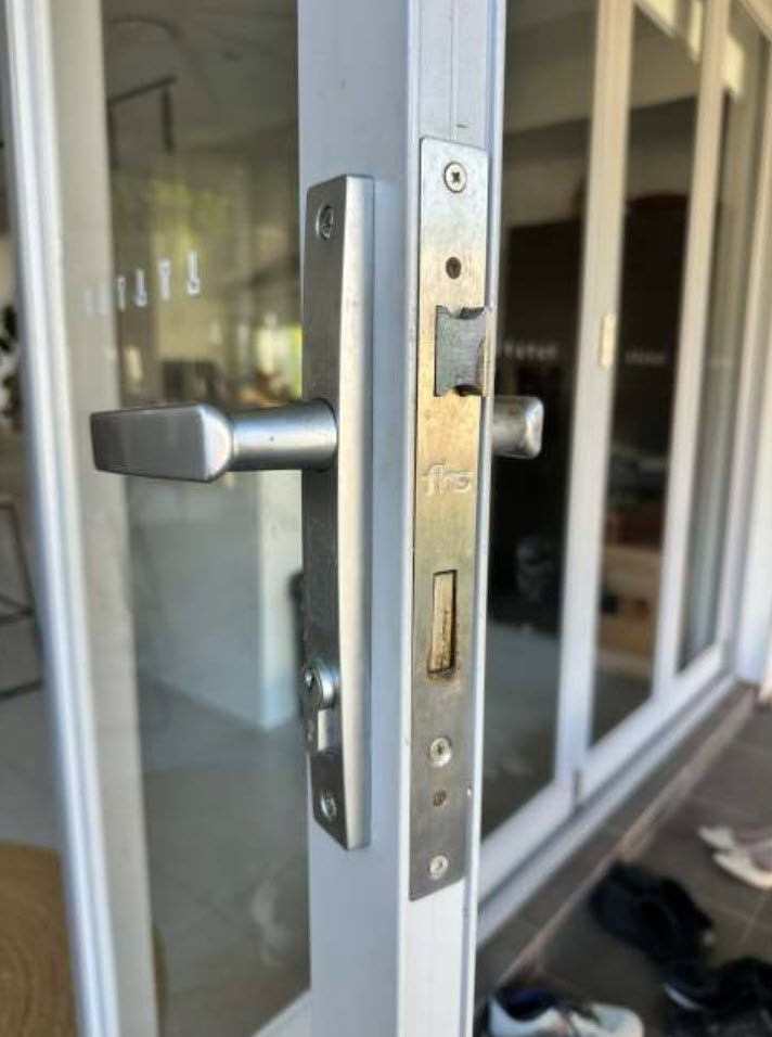 Angled shot of an open aluminium glass door showing the lever on a narrow plate and the mortice faceplate on the narrow door stile