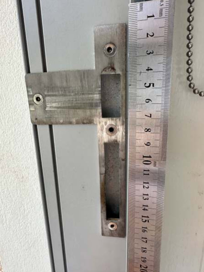 Steel ruler held beside a T-shaped strike plate on the aluminium door frame to show the strike height and where its two pockets sit