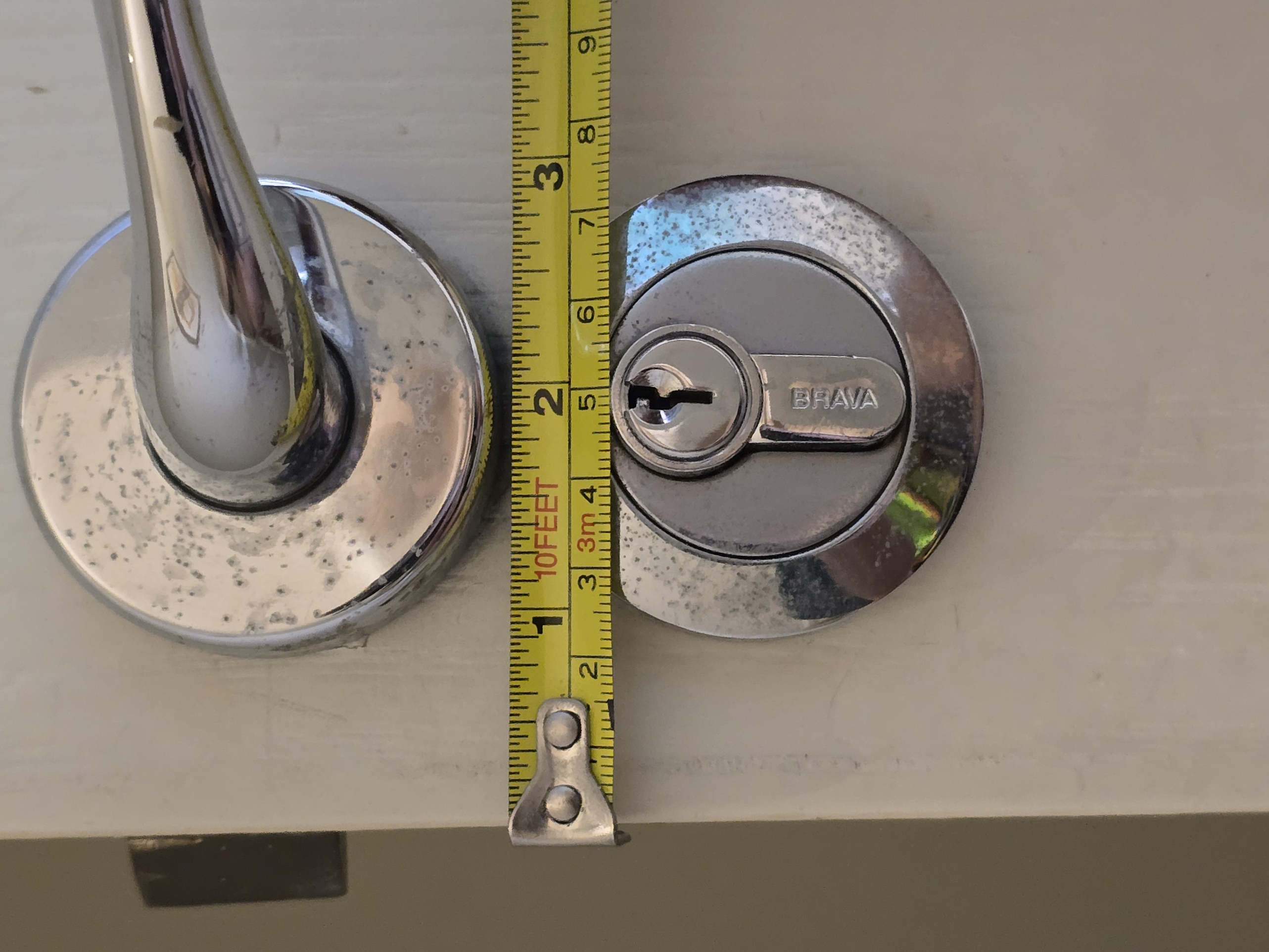 Tape measure hooked on the timber door edge and run across to the centre of a euro cylinder to show the lock backset measurement