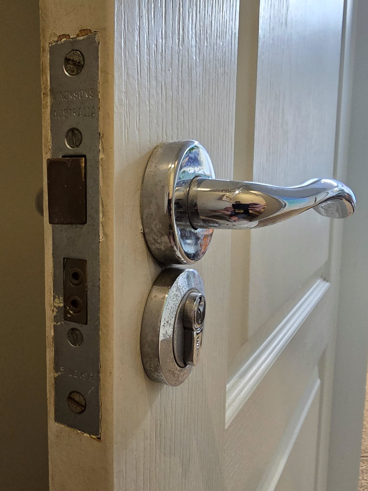 Angled close-up of a chrome lever on a round rose, a euro cylinder escutcheon and a Jacksons Australia 5 lever mortice faceplate on the door edge